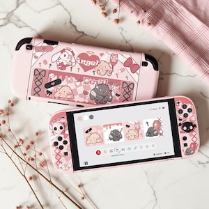 May include: A pink handheld gaming console featuring a custom skin with cartoon characters, hearts, and the text Angel and Devil. The screen displays a matching theme with icons of bunnies, a coffin, and medical motifs in a soft pastel color palette.
