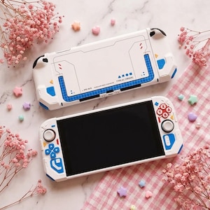May include: A white handheld gaming console with blue and red accents. The back features a grid pattern and the text TYPE-01 ORIGIN. The front includes a black screen, a white directional pad, blue buttons, and red action buttons labeled A, B, X, Y.