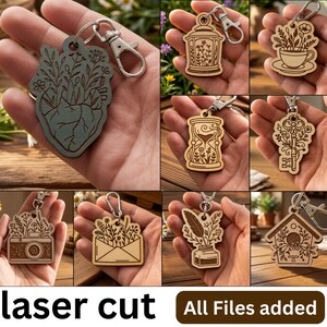May include: A collection of laser-cut wooden keychains featuring various shapes including a heart, lantern, teacup, hourglass, key, camera, envelope, inkwell with a quill, and birdhouse, all decorated with intricate floral line art engravings.