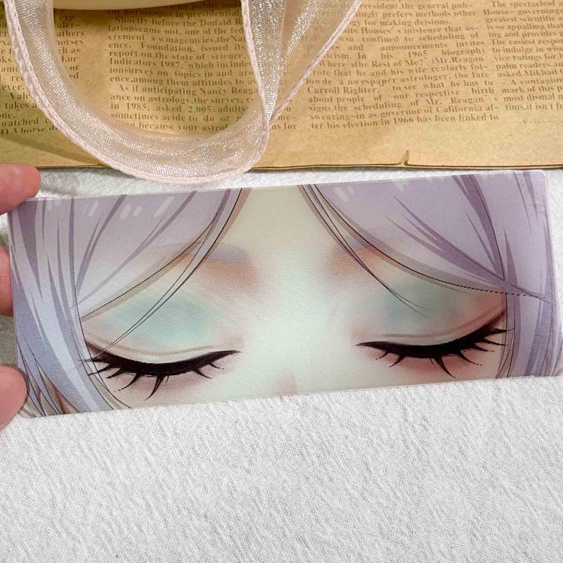 K&ouml;nnte beinhalten: Ein rechteckiges Lesezeichen mit einer detaillierten Illustration geschlossener Augen mit langen schwarzen Wimpern, hellblauem Lidschatten und blasslavendelfarbenem Haar. Das Kunstwerk ist in einem weichen Stil mit sanften Schattierungen gehalten.