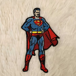 May include: Embroidered patch featuring Superman in his classic costume. The patch shows Superman in a standing pose with his hands on his hips, wearing a blue suit, red cape, and the iconic "S" emblem on his chest.