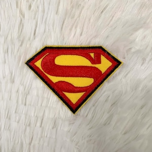 Puede incluir: Parche bordado con el logotipo de Superman. El parche presenta una forma de diamante amarillo con una "S" roja en el centro, delineada en negro. El parche es probablemente para ropa o accesorios.