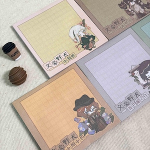 Peut inclure: Une collection de blocs-notes carrés avec des motifs quadrillés et des illustrations de personnages de style anime. Chaque bloc comprend du texte japonais et des accents floraux dans des tons jaune, marron et violet. Une gomme en forme de tasse est incluse.