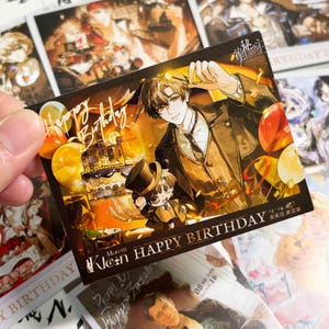 May include: A rectangular birthday card featuring an anime-style illustration of a man in a brown suit and a smaller chibi character in a top hat. The card includes gold text reading Happy Birthday and Moretti Klein HAPPY BIRTHDAY with balloons.