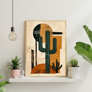 May include: Abstract art print depicting a stylized cactus in teal, orange, and black against a beige backdrop. The artwork is framed in a light wood tone, suggesting a desert theme. The print is displayed on a white shelf with plants.