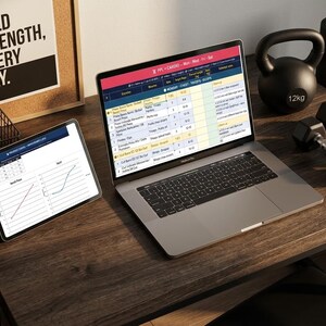 May include: A desk setup featuring a laptop and tablet showing data, a 12kg kettlebell, dumbbells, and a rolled yoga mat. A corkboard with the text "BUILD STRENGTH, EVERY DAY" is also visible.