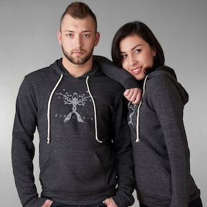 May include: Two people wearing charcoal gray hooded sweatshirts with a white tree design and the text "dream more".