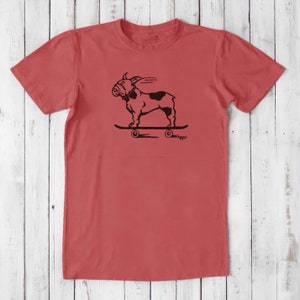 May include: A red t-shirt with a black graphic of a bulldog skateboarding. The bulldog is wearing a collar and has a tongue sticking out. The skateboard has four wheels.