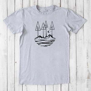May include: A gray t-shirt with a black graphic of three trees, mountains, a crescent moon, and stars. The graphic is in a circle shape.