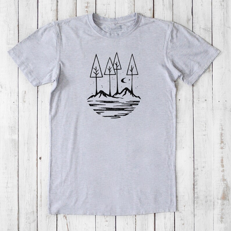 May include: A gray t-shirt with a black graphic of three trees, mountains, a crescent moon, and stars. The graphic is in a circle shape.