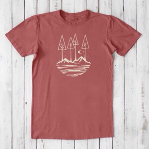 May include: A red t-shirt with a white graphic design of a stylized forest scene with trees, mountains, a crescent moon, and stars.
