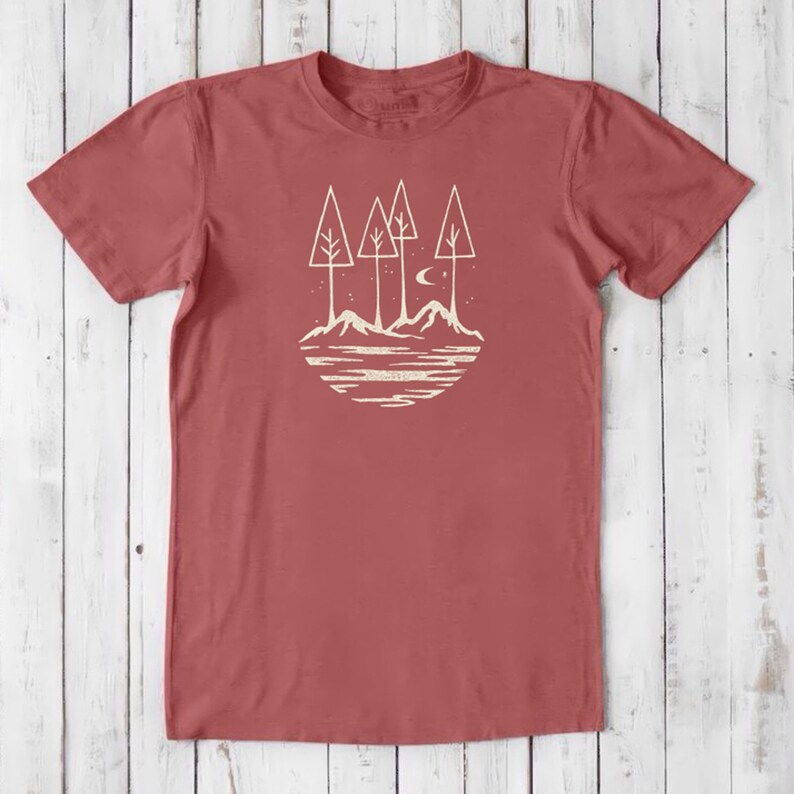 May include: A red t-shirt with a white graphic design of a stylized forest scene with trees, mountains, a crescent moon, and stars.