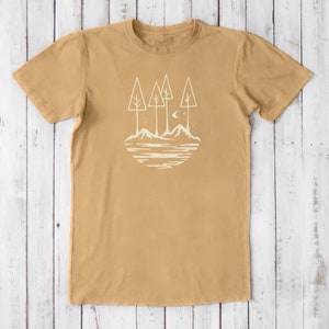 May include: A tan t-shirt with a white graphic of a moon, three trees, and mountains reflected in a lake.