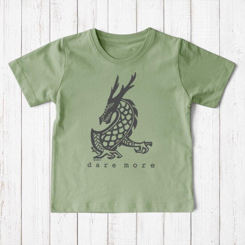 Uni-T kids organic cotton sage green t-shirt featuring a hand-illustrated black dragon graphic and Dare More text.