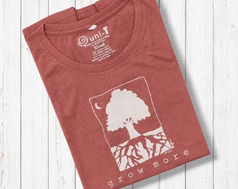 May include: A terracotta-colored short-sleeve t-shirt featuring a white graphic of a tree with visible roots inside a rectangular frame. The text "grow more" is printed below the graphic. The inner neck label displays the brand name uni-T and size XS.