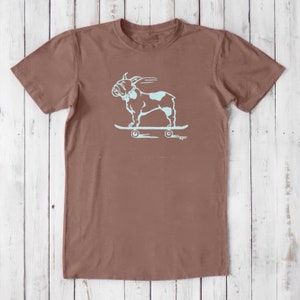 May include: A brown t-shirt with a light blue graphic of a French bulldog skateboarding. The graphic is on the front of the shirt.