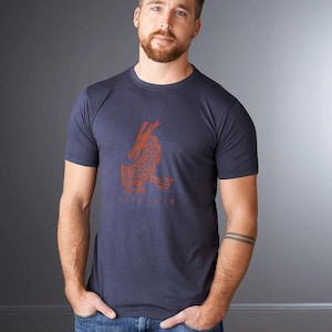 May include: A dark blue short-sleeved t-shirt featuring a rust-colored graphic of a stylized dragon on the chest. The dragon design includes intricate geometric patterns within its body, and the text "DEEP CORE" is printed in small letters below it.