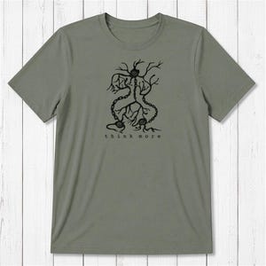May include: An olive green short-sleeve t-shirt featuring a black graphic print of a central circular form with branching, root-like lines and chain-link segments. Below the graphic, the text "think more" is printed in a simple black font.