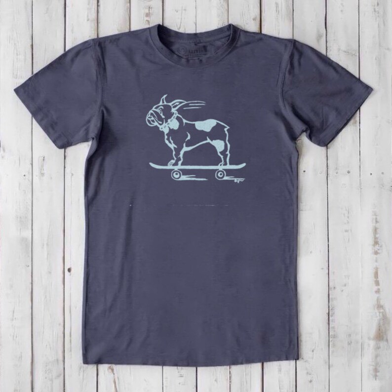 May include: A dark blue t-shirt with a light blue graphic of a French bulldog skateboarding. The graphic is centered on the shirt.