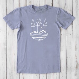 May include: A light blue t-shirt with a white graphic of a moon, stars, and three trees behind a mountain range and a lake.