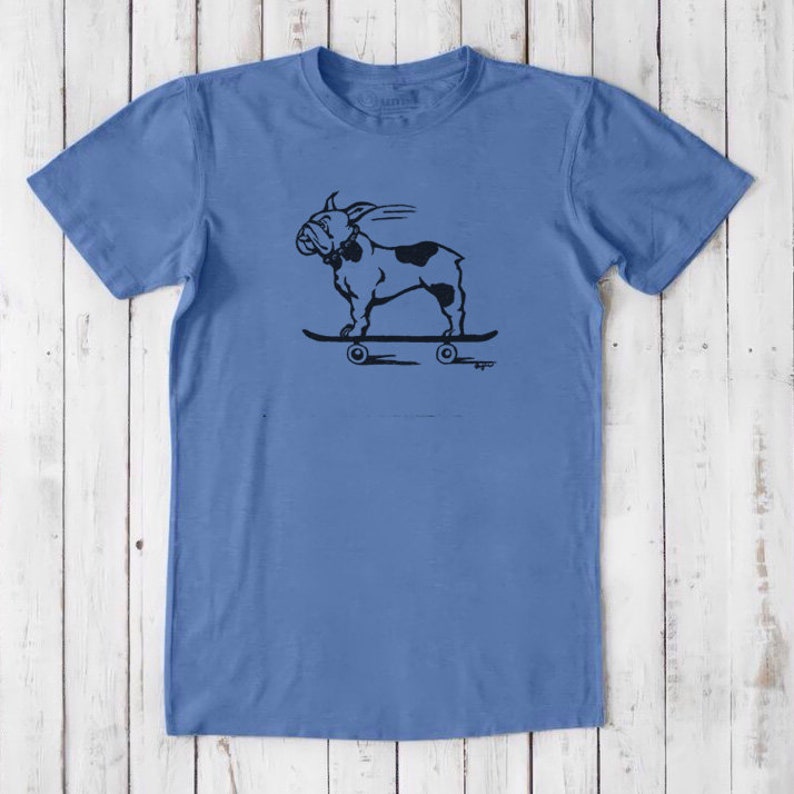 May include: A light blue t-shirt with a black and white illustration of a bulldog riding a skateboard. The bulldog is wearing a collar and has a tongue sticking out. The skateboard has four wheels.