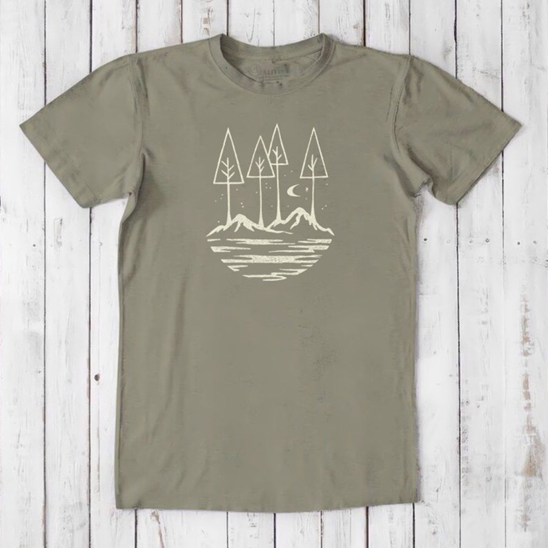 May include: A green t-shirt with a white graphic of a stylized landscape with trees, mountains, and a crescent moon.