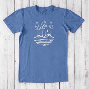 May include: A blue t-shirt with a white graphic of a moon, stars, and three trees on a mountain landscape.