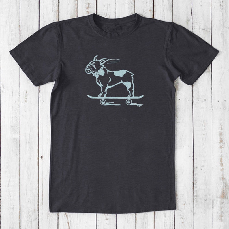 May include: A dark grey t-shirt with a light blue graphic of a French bulldog skateboarding. The graphic is in a vintage style.