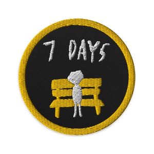 May include: Embroidered patch with a black background and a yellow border. The patch features the text "7 DAYS" in white, above a white stick figure sitting on a yellow bench.