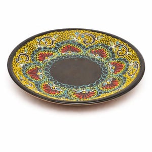 Può includere: Un piatto decorativo in ceramica dipinto a mano con centro e bordo neri. Il piatto presenta un colorato motivo floreale in giallo, rosso e blu. Il design è simmetrico e dettagliato, aggiungendo un tocco artistico alle stoviglie.