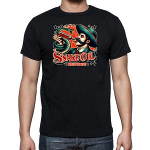 Può includere: T-shirt nero con un'illustrazione in stile vintage. La grafica raffigura un uomo con i baffi e un cappello, che tiene in mano una bottiglia con un serpente avvolto. È presente anche il testo "SNAKE OIL" e "RELEASE THE BEAST".