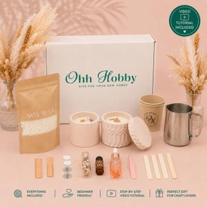 Puede incluir: Un kit para hacer velas que incluye una caja blanca con la etiqueta Ohh Hobby, una bolsa de cera de soja, dos recipientes de cerámica, una jarra de metal, un vaso de papel, un frasco de aceite, flores secas, pinzas y palitos de madera.