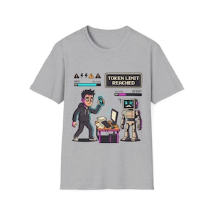 Könnte beinhalten: Ein graues T-Shirt mit einer Grafik, die eine Person und einen Roboter an einem Schreibtisch zeigt, sowie den Text TOKEN LIMIT REACHED. Das Design enthält Gesundheitsbalken für DEV und AI BOT, Warnsymbole und einen Computer mit Papieren.