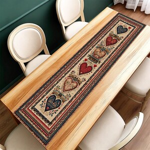 May include: A rectangular table runner featuring a cream backdrop and a heart motif. The hearts are in red and blue hues, adorned with floral and scroll patterns. The runner is framed by a red and navy blue border.