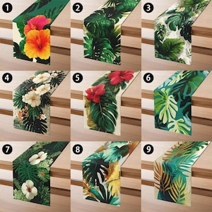 Könnte beinhalten: Neun dekorative Tischläufer mit tropischen Blumen- und Blattmustern. Die Läufer weisen leuchtende Farben auf, darunter Grün, Gelb, Rot und Weiß, mit verschiedenen botanischen Mustern. Jeder Läufer wird auf einer Holzoberfläche präsentiert.