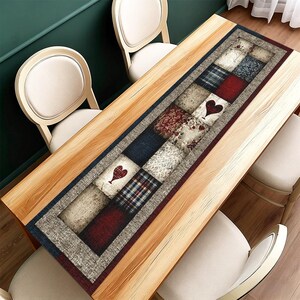 May include: A rectangular table runner with a patchwork design featuring squares of various patterns and colours, including red hearts, plaid, and floral prints. The runner is bordered by a grey fabric and placed on a wooden table.