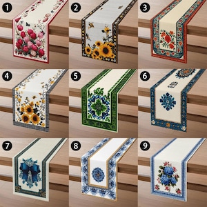 May include: Nine decorative table runners with various floral and geometric designs. The runners feature a range of colors, including red, pink, yellow, blue, and green, with detailed patterns and borders. Each runner is displayed on a wooden surface.
