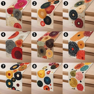 May include: A collection of nine decorative table runners with colorful, abstract floral designs. Each runner features a different pattern of circular shapes in various colors, including red, orange, yellow, green, and blue, on a neutral background. The runners are displayed on a wooden surface.