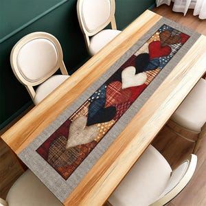 May include: A table runner featuring a heart design in shades of red, white, blue, and brown, with patchwork and plaid patterns. The runner is framed by a grey border and rests on a wooden table. The table runner's length is approximately 150 cm.