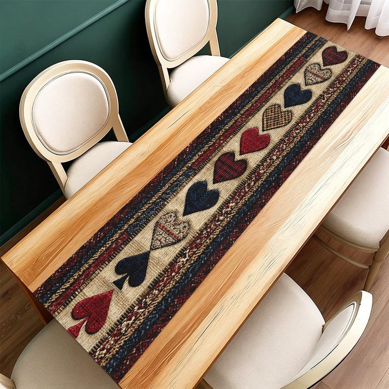 May include: A rectangular table runner with a repeating pattern of hearts and spade suit symbols. The runner features a mix of red, blue, and tan colours with a textured design. The runner is placed on a light wood table.
