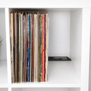 Könnte beinhalten: Eine Sammlung von Schallplatten, die vertikal in einem weißen Würfelregal aufbewahrt werden. Die Platten haben verschiedene bunte Cover mit sichtbarem Text, darunter Erasure Live in Hamburg Collection. Ein schwarzer Trenner aus Metall steht dahinter.