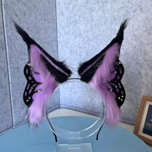 Puede incluir: Una diadema con dos grandes alas de mariposa puntiagudas. Las alas están hechas de piel sintética negra y morada clara con patrones de venas negras y pequeños diamantes de imitación transparentes incrustados en toda la superficie.