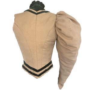 May include: A beige sleeveless bodice with a single, large, puffed sleeve. The bodice has a green velvet collar and trim with black velvet ribbon accents.
