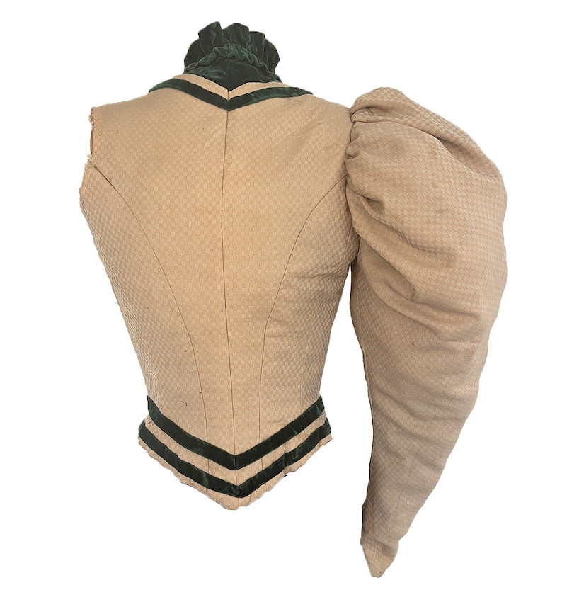 May include: A beige sleeveless bodice with a single, large, puffed sleeve. The bodice has a green velvet collar and trim with black velvet ribbon accents.