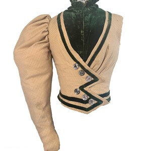 May include: A vintage jacket in beige and green with a high collar and a single long sleeve. The jacket has a green velvet lining and is trimmed with black velvet ribbon.