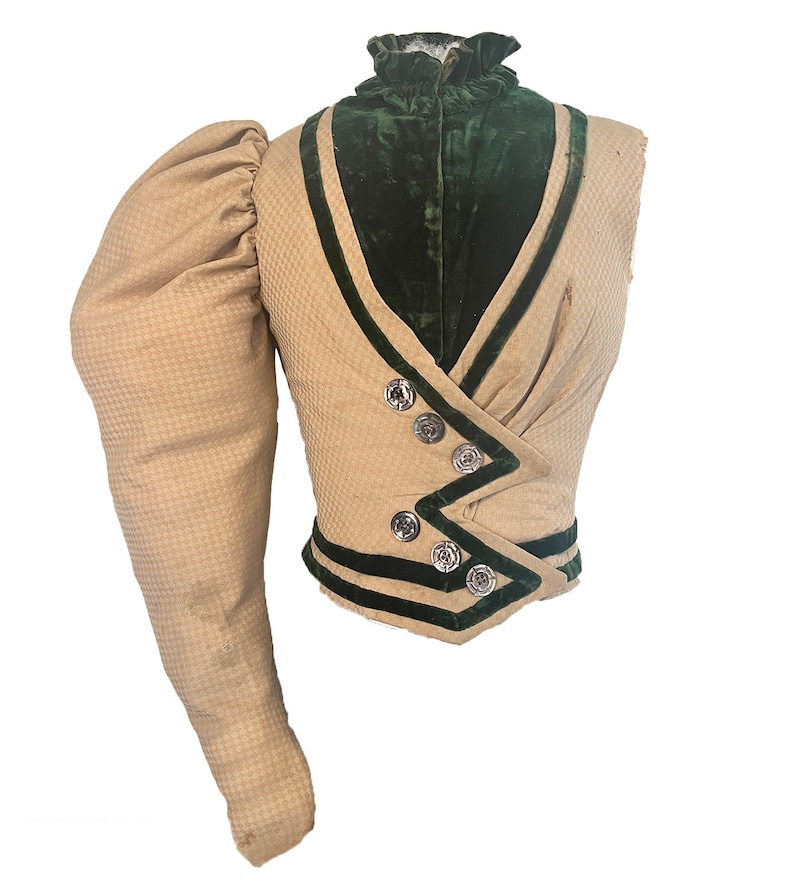 May include: A vintage jacket in beige and green with a high collar and a single long sleeve. The jacket has a green velvet lining and is trimmed with black velvet ribbon.