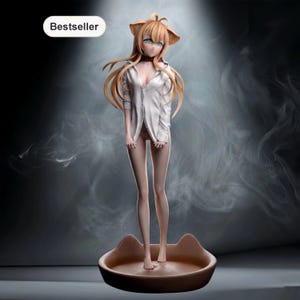 Puede incluir: Figura de una mujer con orejas de gato, vestida con una camisa blanca, de pie en una base marrón con forma de gato. La figura tiene pelo largo, castaño claro y ojos verdes. La palabra "Bestseller" está en un óvalo blanco.