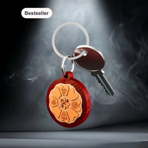 Op de afbeelding: Een rode en oranje houten sleutelhanger met een bloemdesign en een zilveren sleutelring. Een sleutel is bevestigd. Het woord "Bestseller" staat in een wit kader linksboven.