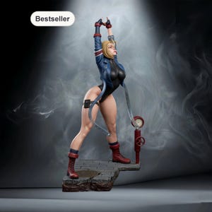 以下が含まれることがあります： 黒いボディスーツと青いジャケットを着た女性キャラクターの精巧なフィギュア。金髪、赤いブーツ、脚用ホルスターが特徴です。腕を上げたポーズで、赤い産業要素に接続されています。「Bestseller」の文字が左上にあります。