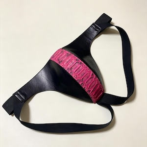 May include: A black faux leather jockstrap featuring a central panel with a vibrant pink snakeskin-textured pattern. The garment is constructed with smooth black panels and includes black elastic straps that form the waistband and leg loops.